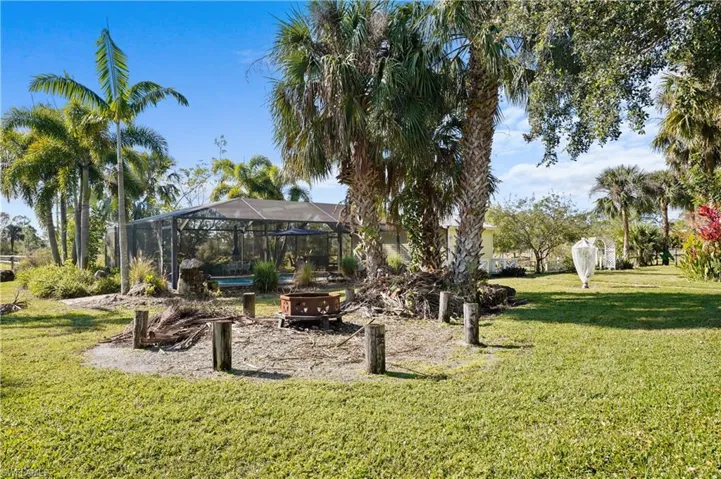 Firepit and fiew of screened pool cage with waterfall and pool house. Lots of fruit trees.