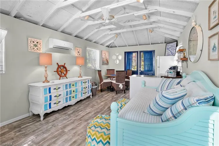 Living room with lofted ceiling with beams, ceiling fan, a wall mounted air conditioner, and hardwood / wood-style floors