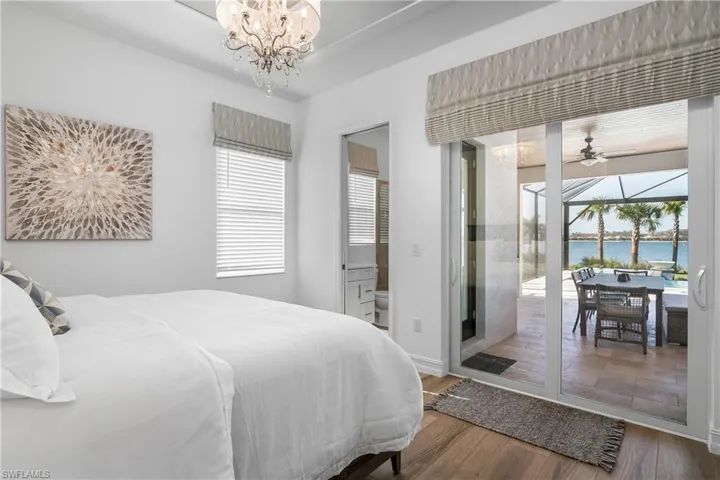 Bedroom with a sunroom, wood finished floors, a water view, access to outside, and a chandelier
