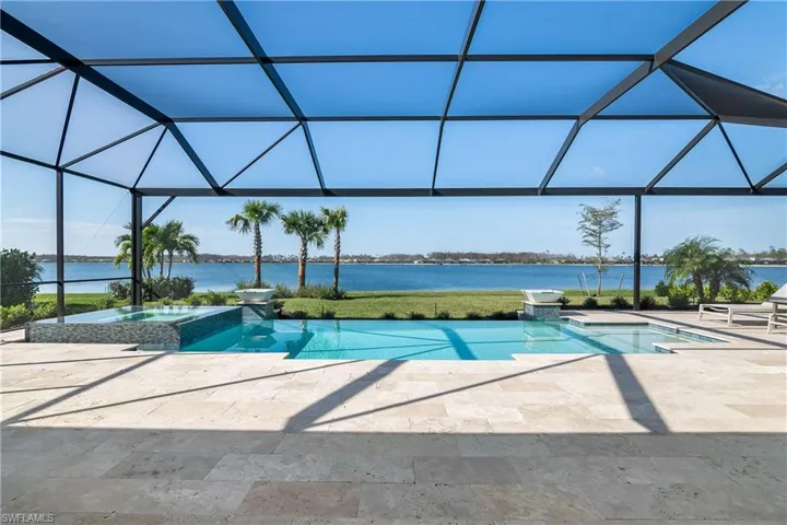 View of pool featuring a pool with connected hot tub, glass enclosure, a water view, a patio, and a sunroom