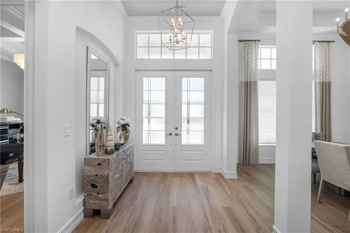 Foyer with a chandelier, crown molding, light wood finished floors, arched walkways, and plenty of natural light