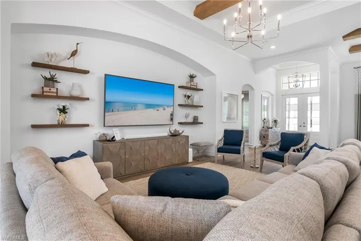 Living area featuring arched walkways, french doors, wood finished floors, ornamental molding, and a chandelier