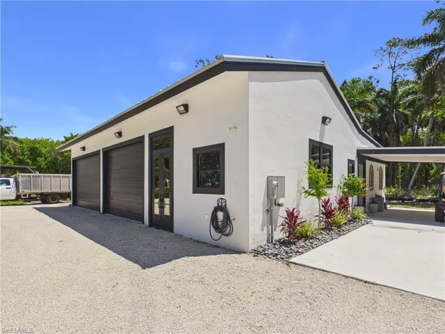 Modern white stucco exterior with a multi-car garage featuring dark wood-look doors, a covered carport, and accent landscaping