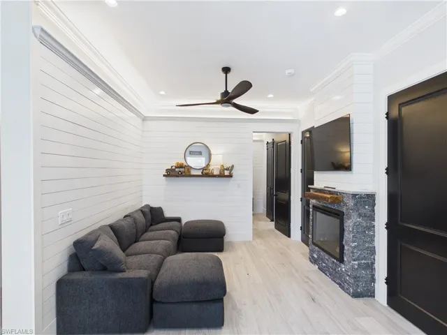 Living area featuring white shiplap walls, light wood-finish flooring, and a contemporary ceiling fan