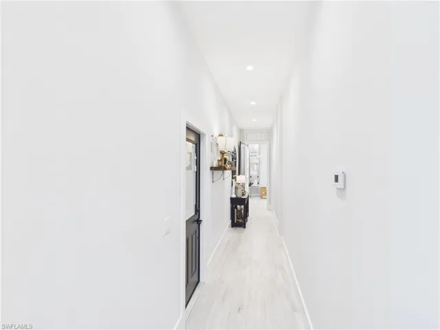 Hallway featuring recessed lighting, light wood-finish flooring, white walls, and a black paneled door