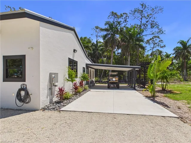 White stucco exterior with black-framed windows, a covered carport, and a gravel driveway