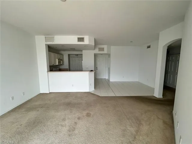 Unfurnished living room with light carpet, arched walkways, and light tile patterned flooring
