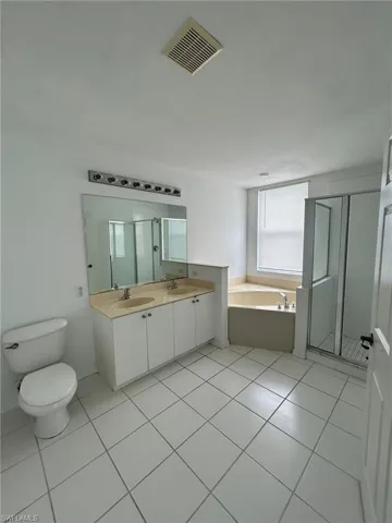 Full bathroom featuring light tile patterned floors, a stall shower, a bath, and double vanity