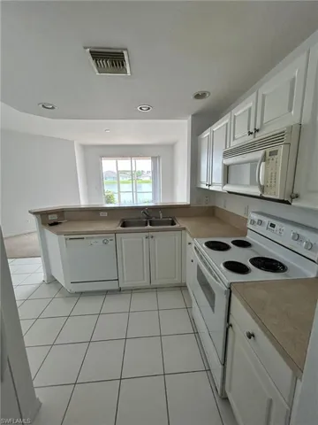 Kitchen with white appliances, white cabinets, a peninsula, light tile patterned floors, and recessed lighting