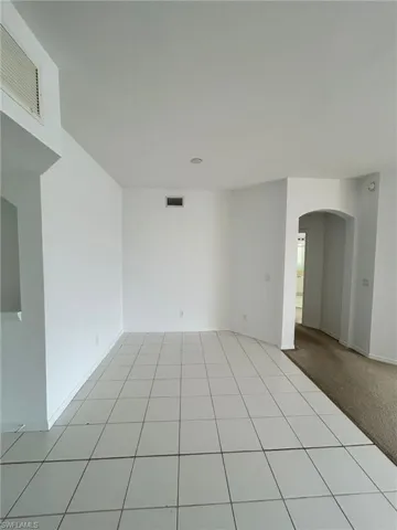 Empty room featuring arched walkways, light tile patterned floors, and light carpet