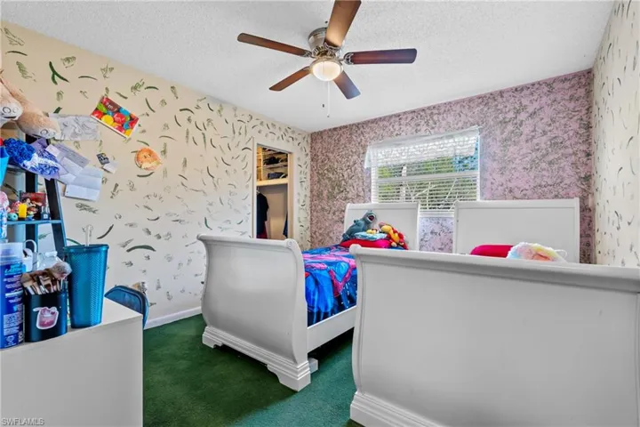 Bedroom featuring wallpapered walls, a textured ceiling, dark colored carpet, and a ceiling fan