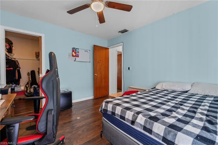 Bedroom featuring dark wood-style floors, a spacious closet, a ceiling fan, a desk, and a textured ceiling