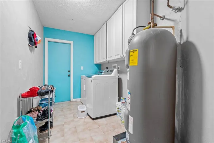 Laundry room with electric water heater, cabinet space, washing machine and clothes dryer, and a textured ceiling