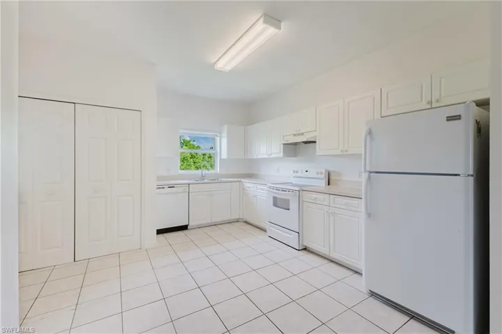 Kitchen with white appliances, white cabinetry, light countertops, light tile patterned floors, and under cabinet range hood