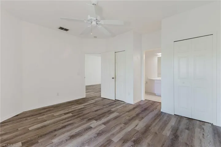 Unfurnished bedroom with wood finished floors, a ceiling fan, two closets, and connected bathroom