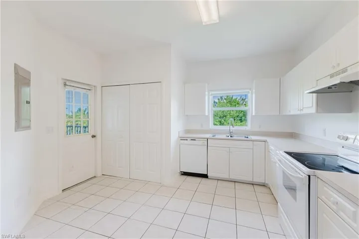 Kitchen featuring white appliances, light countertops, light tile patterned floors, white cabinets, and under cabinet range hood