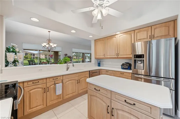 Kitchen with light cabinetry, sink, stainless steel fridge, light tile patterned floors, and electric range