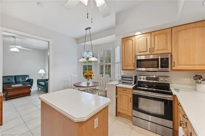 Kitchen featuring ceiling fan, hanging light fixture, kitchen island, stainless steel appliances, and light tile patterned flooring