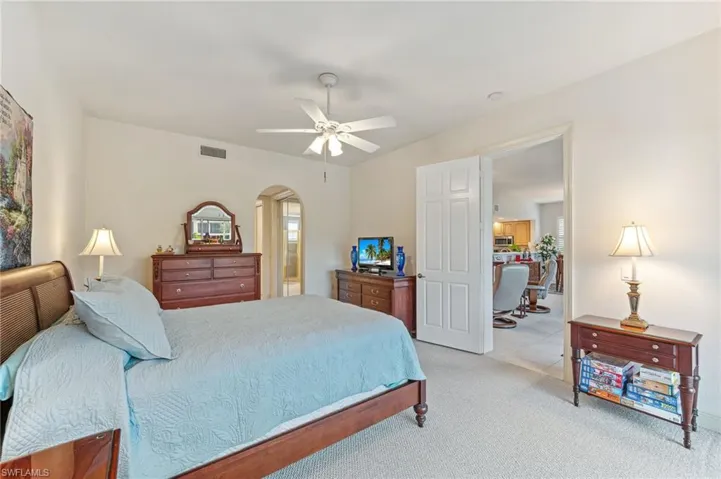 Primary bedroom with light colored carpet, ceiling fan, and ensuite bathroom