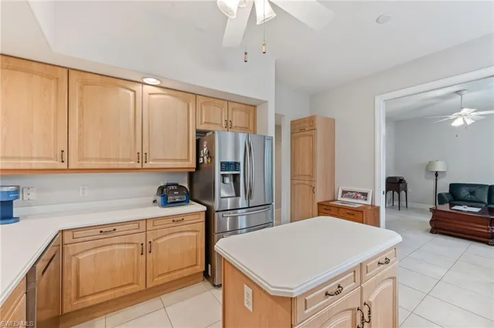 Kitchen with light tile patterned flooring, a kitchen island, light brown cabinetry, stainless steel fridge, and ceiling fan
