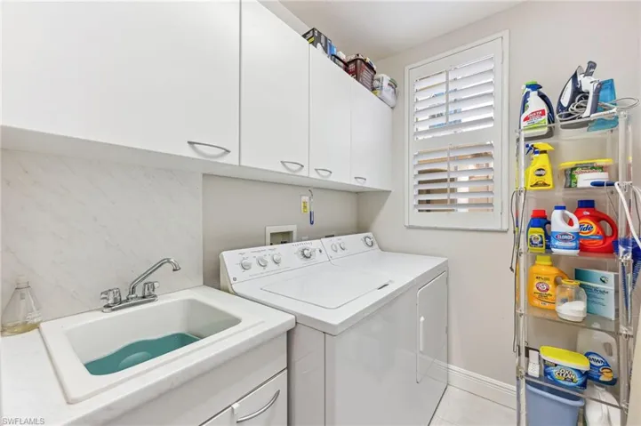 Laundry room inside residence with cabinets, light tile patterned flooring, sink, and washer and clothes dryer