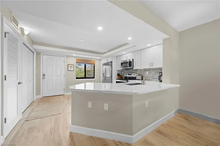 Kitchen with light stone countertops, tasteful backsplash, appliances with stainless steel finishes, light wood-type flooring, and recessed lighting