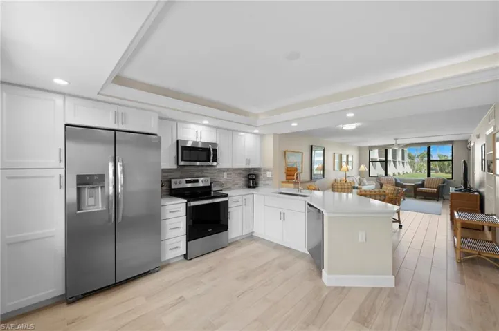 Kitchen with appliances with stainless steel finishes, open floor plan, white cabinets, backsplash, and a peninsula