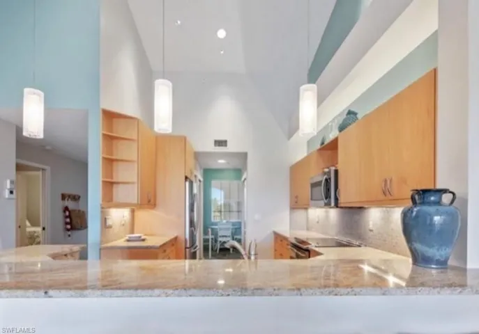 Kitchen featuring stainless steel appliances, open shelves, a high ceiling, backsplash, and light stone counters