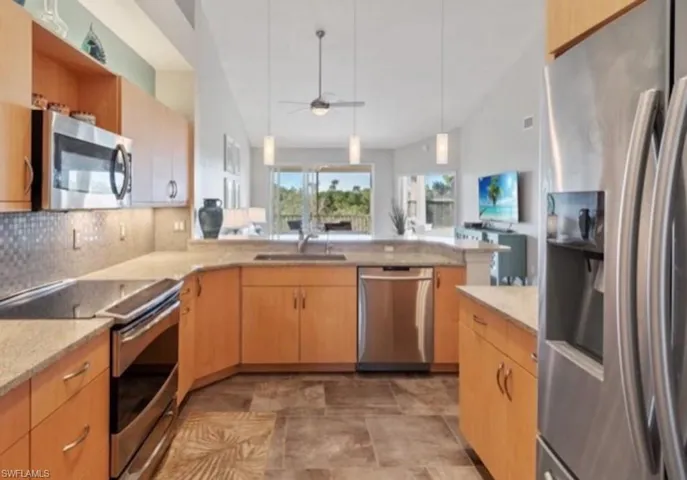 Kitchen featuring appliances with stainless steel finishes, decorative backsplash, open floor plan, a ceiling fan, and hanging light fixtures