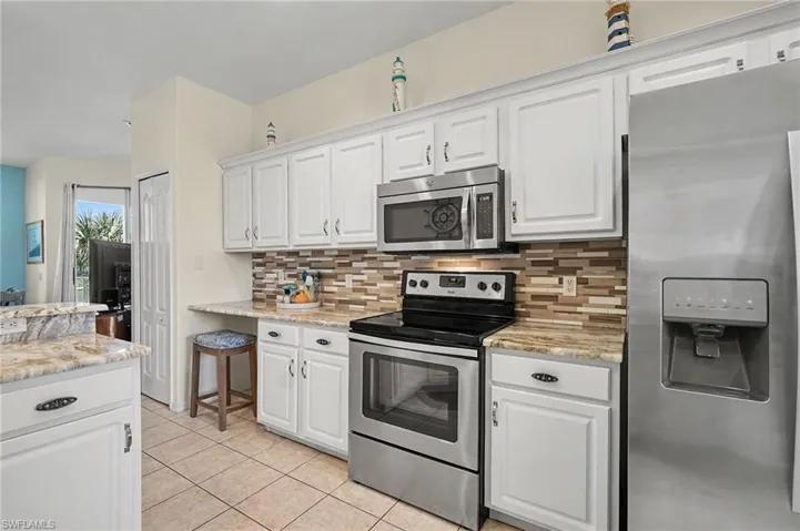 Kitchen featuring stainless steel appliances, white cabinetry, light stone counters, and light tile patterned floors