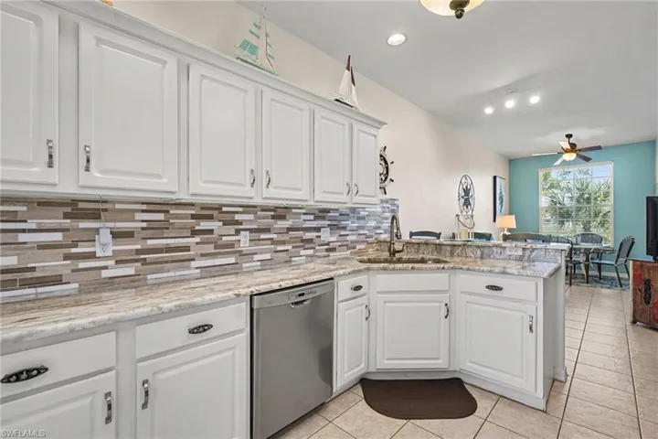 Kitchen with white cabinets, stainless steel dishwasher, a peninsula, a ceiling fan, and light stone counters