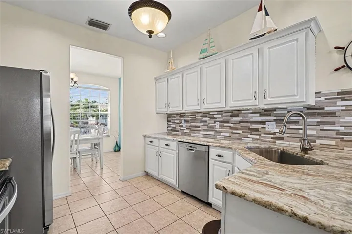 Kitchen with white cabinetry, stainless steel appliances, light stone countertops, and light tile patterned floors
