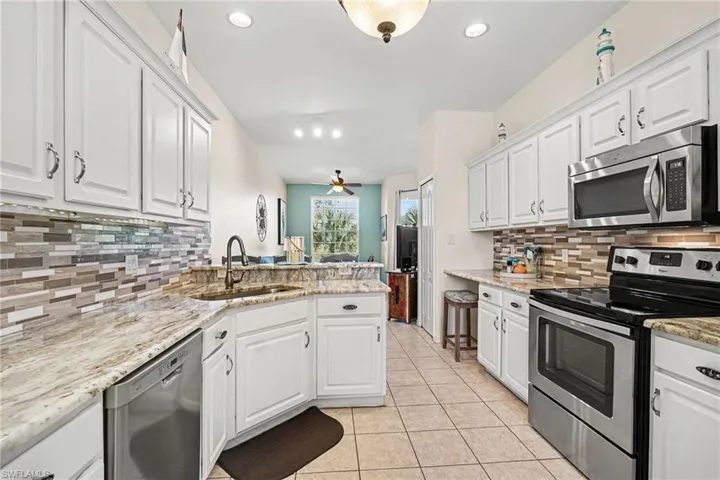 Kitchen featuring stainless steel appliances, white cabinetry, light stone counters, backsplash, and recessed lighting