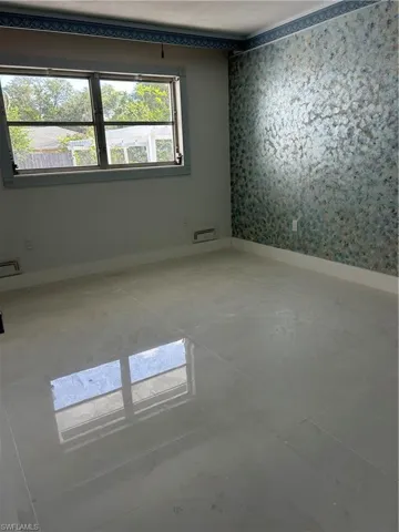 Spacious room featuring polished tile flooring, a large window, a decorative accent wall, painted walls, and crown molding