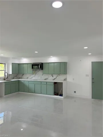 Kitchen featuring mint green cabinetry, a built-in microwave, and marble-look countertops with a matching backsplash