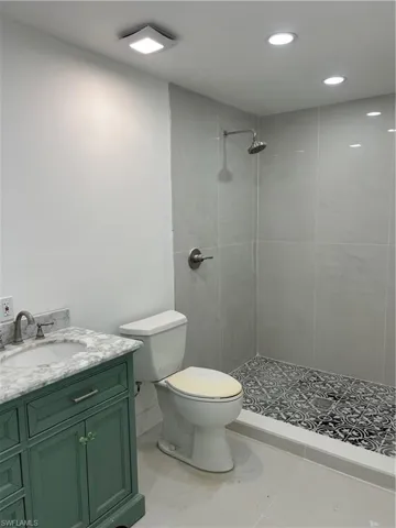 Bathroom featuring a green vanity with a marble-finish countertop, a single-handle faucet, a walk-in shower with large format wall tiles, and a decorative tile shower pan