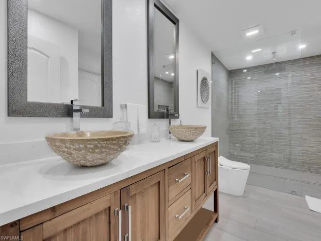 Bathroom with a tile shower, dual bowl vanity, and toilet