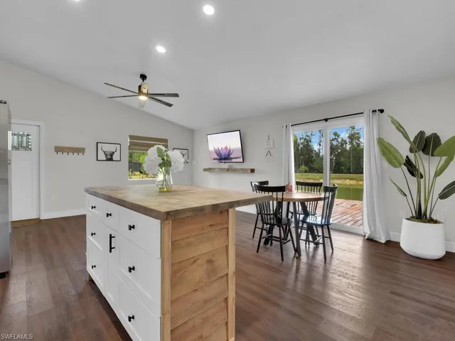 Kitchen with vaulted ceiling, dark hardwood / wood-style flooring, wood counters, ceiling fan, and a center island