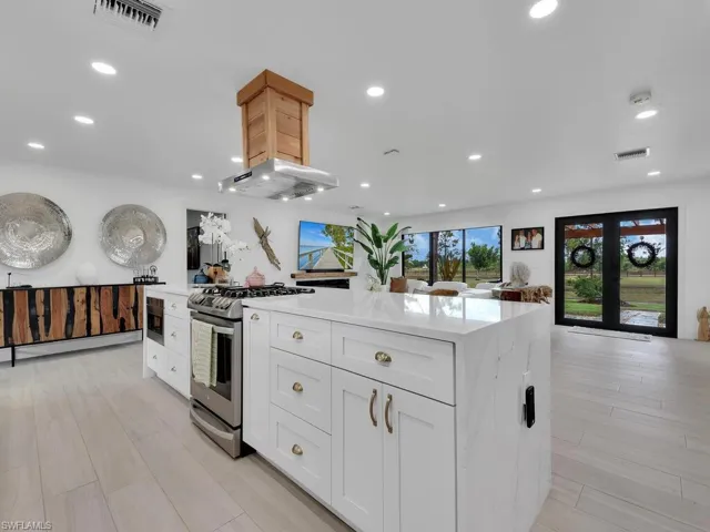 Kitchen featuring a center island, light hardwood / wood-style floors, stainless steel gas stove, white cabinets, and ventilation hood