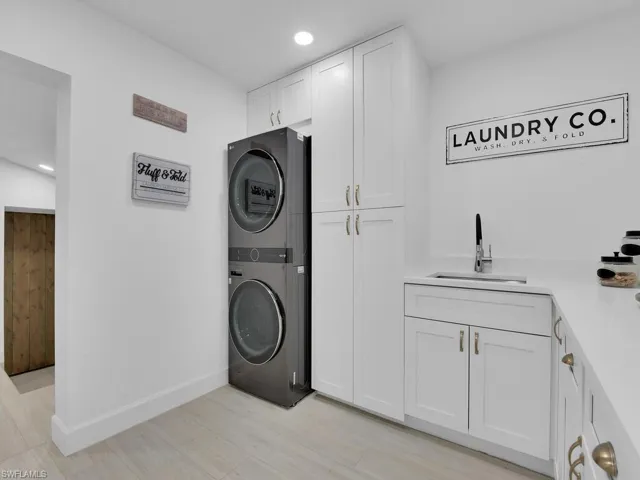 Clothes washing area featuring stacked washer and clothes dryer, cabinets, sink, and light wood-type flooring