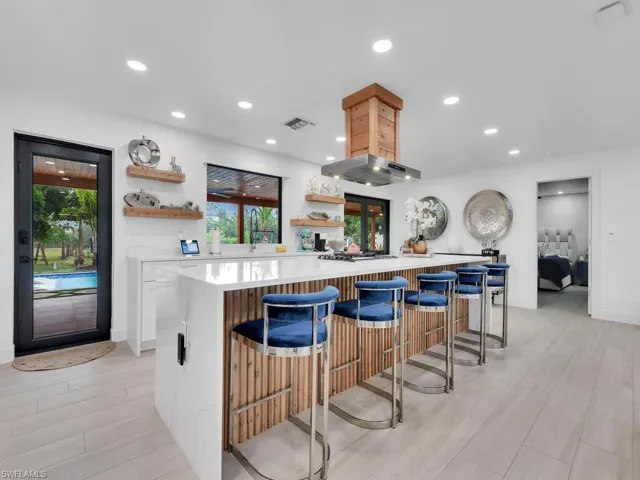 Kitchen featuring light hardwood / wood-style floors, a kitchen island, white cabinets, exhaust hood, and a breakfast bar
