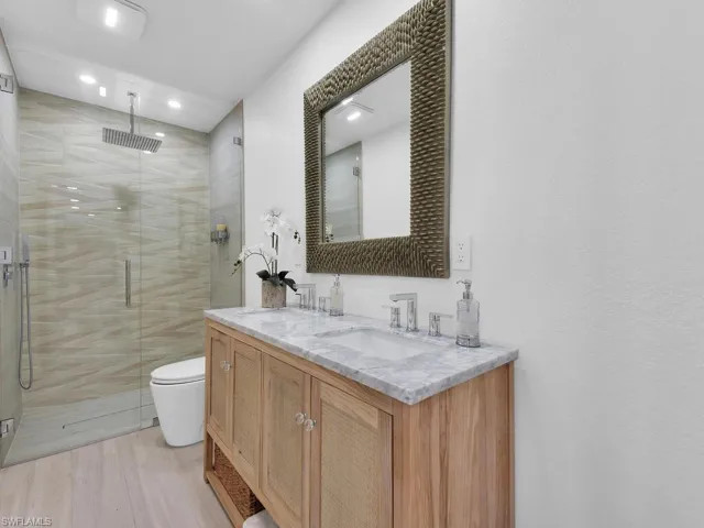 Bathroom with a shower with door, tile walls, toilet, and vanity