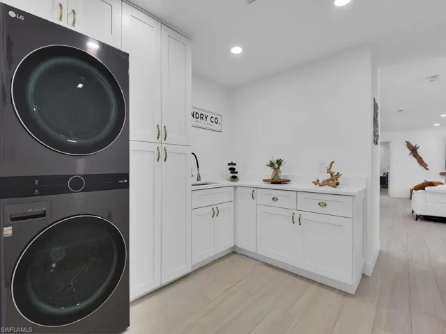 Clothes washing area featuring stacked washer and clothes dryer, sink, light hardwood / wood-style flooring, and cabinets