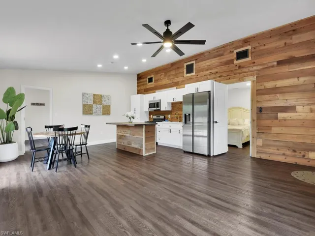 Kitchen with vaulted ceiling, dark hardwood / wood-style floors, white cabinetry, appliances with stainless steel finishes, and wooden walls