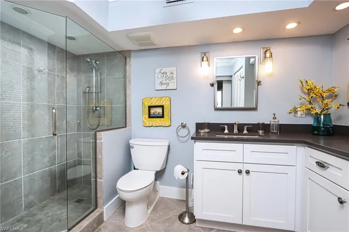 Bathroom featuring a shower with door, toilet, tile floors, and large vanity