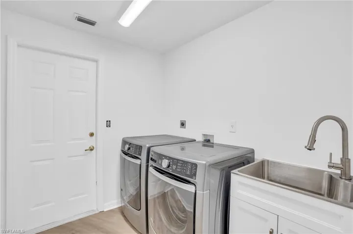 Laundry area with washer and clothes dryer, cabinets, light hardwood / wood-style floors, and sink