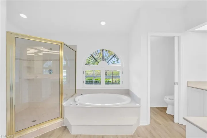 Full bathroom with independent shower and bath, vanity, toilet, and hardwood / wood-style floors
