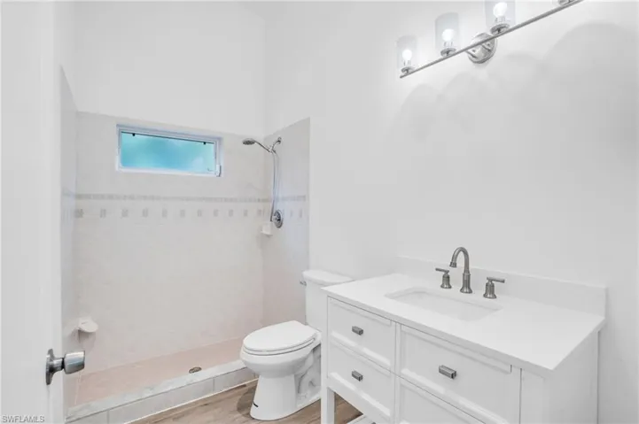 Bathroom with wood-type flooring, tiled shower, vanity, and toilet