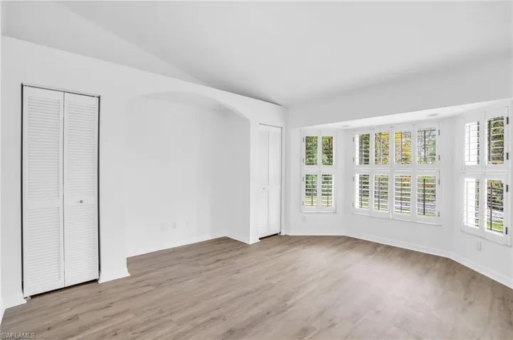 Unfurnished bedroom featuring light wood-type flooring, two closets, multiple windows, and lofted ceiling