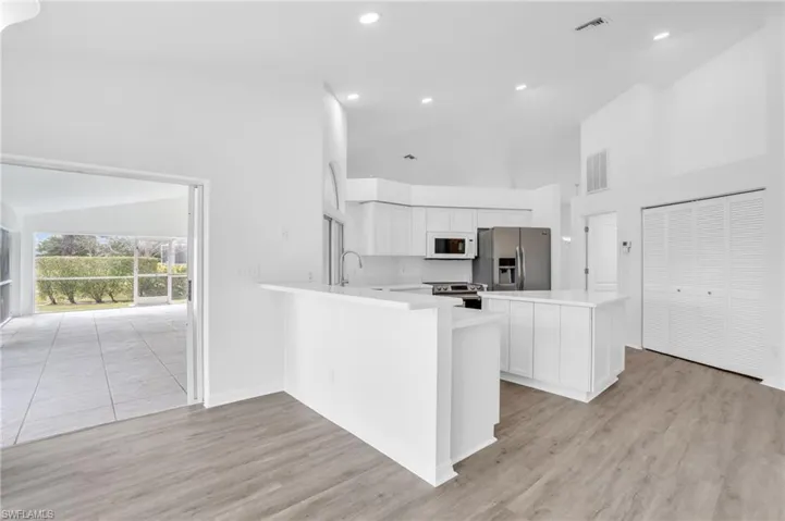 Kitchen featuring light hardwood / wood-style floors, white cabinetry, high vaulted ceiling, kitchen peninsula, and stainless steel appliances